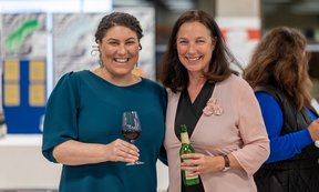 Zwei lächelnde Frauen stehen nebeneinander und halten ein Glas Sekt in der Hand.
