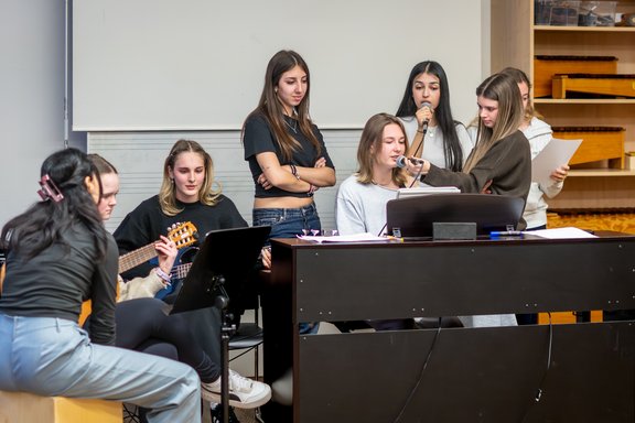 Eine Schülerinnen-Band macht Musik: Eine Person spielt am E-Piano, eine spielt Gitarre, eine spielt Cajon und mehrere singen.