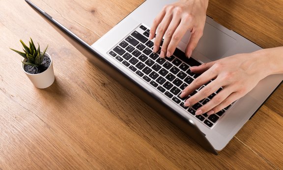 Frau arbeitet mit Laptop auf altem Holztisch in modernem Café oder Loft. Mix aus Bürobedarf und Gadgets auf einem hölzernen Schreibtischhintergrund. Kopierraum.