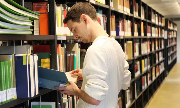 Student in der Bibliothek blättert in einem Buch