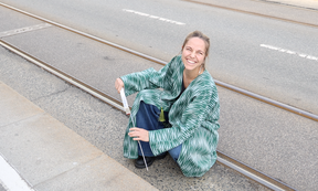 Person sitzt auf der Straße und vermisst Bordsteinkante mit Maßstab aus Holz