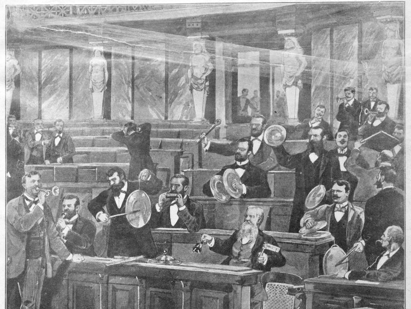 Eine historische Schwarz-Weiß-Illustration zeigt eine turbulente Szene in einem prächtigen Parlamentssaal, in dem Männer in formeller Kleidung mit Trompeten, Glocken und Topfdeckeln lautstark Lärm machen.