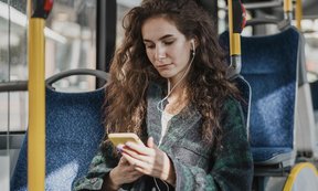 Ein Person sitzt in einem Bus und blickt auf ein Mobiltelefon.