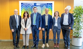 Sechs Personen stehen in einer Reihe vor einem Bild von Erwin Schrödinger und blicken in die Kamera