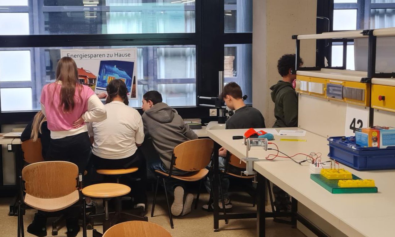 Sechs Schüler:innen arbeiten mit dem Rücken zur Kamera gemeinsam an einem Tisch