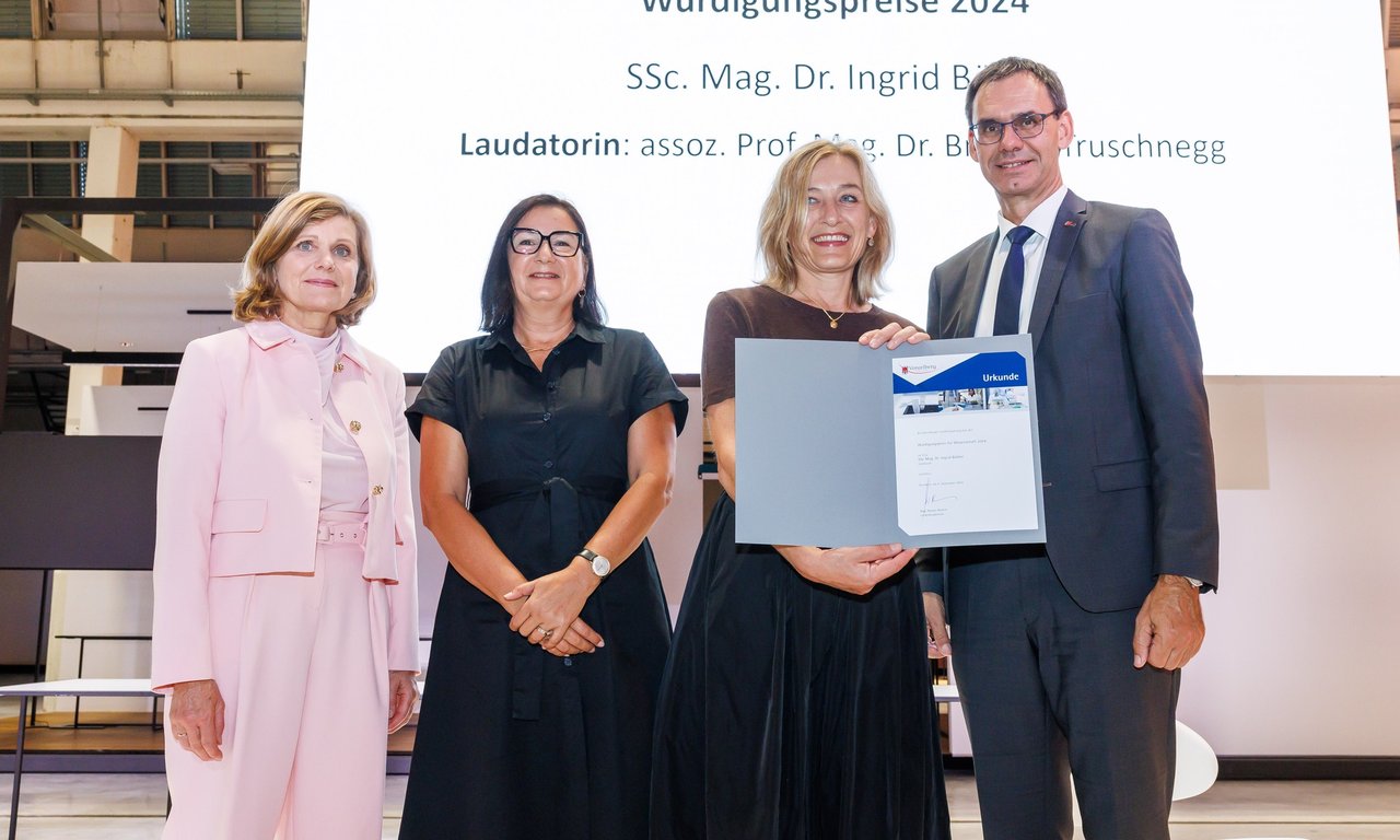 Vier Personen auf einer Bühne, im Hintergrund eine Leinwand